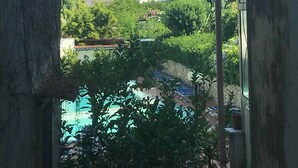 A view of a building with multiple windows and a balcony, surrounded by greenery and a pool area.