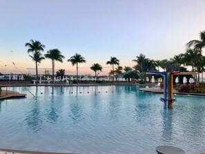 A swimming pool with lounge chairs and umbrellas, surrounded by palm trees. - Harborside (Paradise Island)