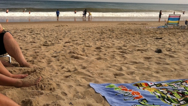 Una playa arenosa con algunas personas y una toalla colorida sobre la arena.