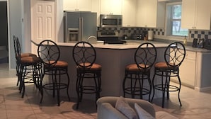 Una cocina moderna con armarios blancos, una isla central con taburetes y un rincón comedor con sofá.