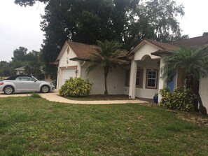 Ein zweistöckiges Haus mit weißer Fassade, braunem Dach und einer Garage. Ein silbernes Auto steht auf der Auffahrt.