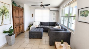 A living room with a grey sectional sofa, a wooden cabinet, and a large window.