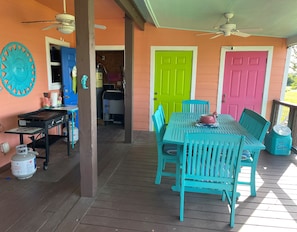Une véranda couverte avec une table et des chaises en bois, un ventilateur de plafond et des portes aux couleurs vives.