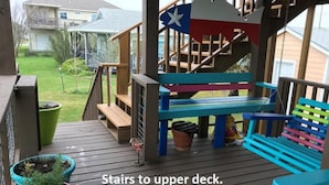 Eine Holzterrasse mit einer Treppe zu einem erhöhten Deckbereich, ausgestattet mit einer Bank und einer Flagge.