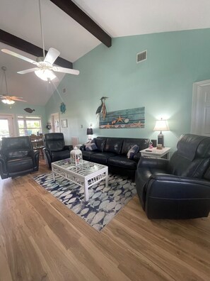 A living room with a black leather sofa, a glass coffee table, and a ceiling fan.