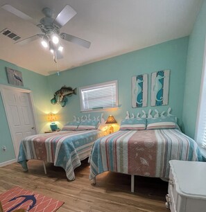 A bedroom with two beds, a ceiling fan, a window with blinds, and a door.