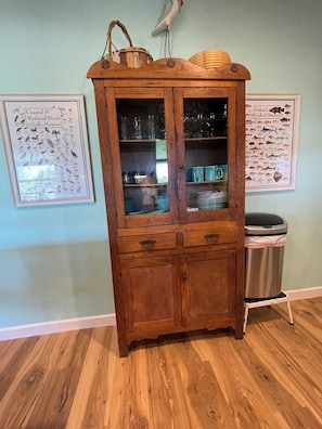 A wooden cabinet with glass doors, a trash can, and two framed posters on the wall.