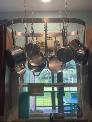 A kitchen with hanging pots and pans, a window with a view of the outdoors, and a teal-colored towel on the counter.