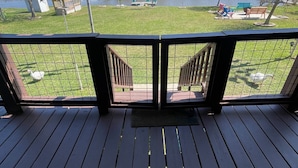 Eine Holzterrasse mit Blick auf einen See, umzäunter Bereich und Gartenmöbel.