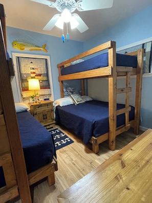 Une chambre avec des lits superposés, une commode en bois, une lampe et un ventilateur de plafond.