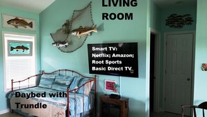 Ein Wohnzimmer mit Tagesbett und zugeschobener Unterbett, einem kleinen Fernseher mit Streaming-Angeboten und einer Wand mit Fischmotiven.