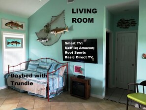 Sala de estar con una cama tipo diván y literas, un televisor pequeño mostrando servicios de transmisión, y un mural con motivos de peces.