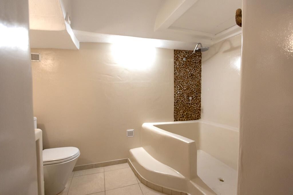 Een badkamer met toilet, bad en douchegedeelte met een patroon in de wand.