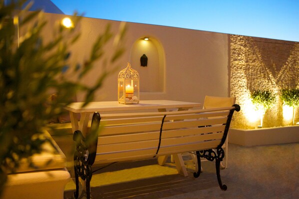 Un espace extérieur aménag é avec une table et des bancs, une lanterne et un mur agrémenté d’une fenêtre en arc de cercle.