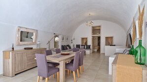 Amplia sala de estar con techo abovedado, mesa de comedor de madera con sillas moradas, un sofá y una cocina con alacena de madera y un espejo.