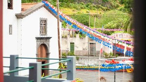 Vista de um edifício branco com uma pequena janela e porta, uma escadaria e um ornamento colorido na colina ao fundo.