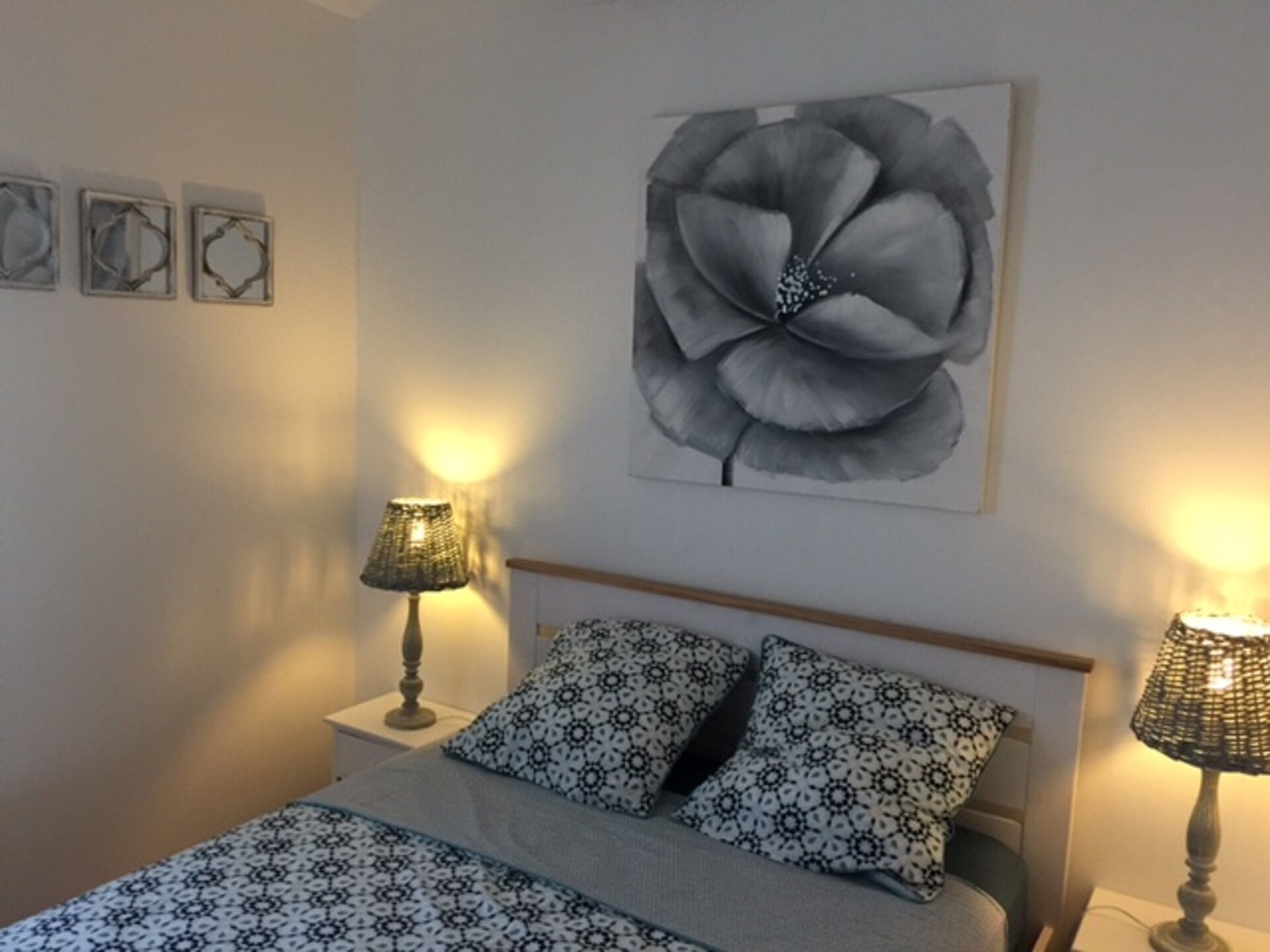 Una camera da letto con un letto, due lampade ai comodini, un grande quadro floreale sulla parete e tre opere d'arte più piccole sopra il letto.
