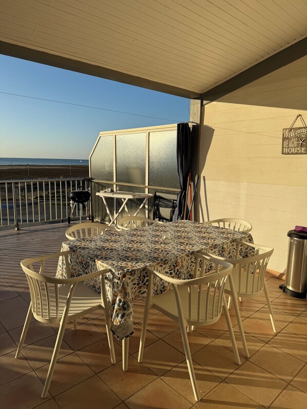 Un patio couvert avec une table et des chaises, un barbecue et une vue sur la plage.