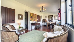 Een ruime woonkamer met een groen vloerkleed, houten meubels, een eethoek met een tafel en stoelen, en een groot raam met uitzicht.
