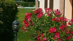Een gebouw met twee verdiepingen, een beige gevel en bruine accenten, omringd door een verzorgde tuin met roze bloemen.