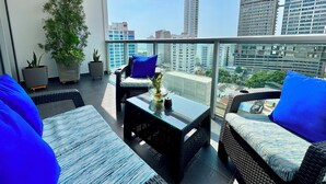 A balcony with wicker furniture, potted plants, and a city view.