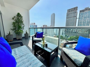Ein Balkon mit Korbmöbeln, Blumentöpfen und Blick auf die Stadt.