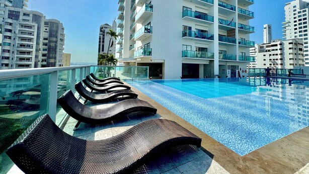 A rooftop swimming pool with lounge chairs, surrounded by high-rise buildings.