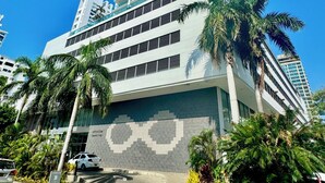 A modern high-rise building with a patterned facade, palm trees, and a clear blue sky.
