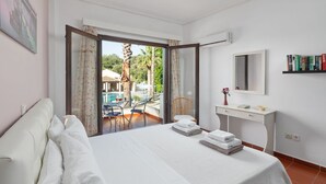Habitación de hotel con cama, escritorio, silla, mesita y balcón con piscina y sillas.