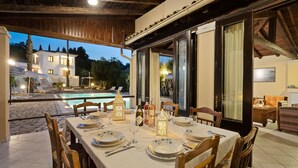 Un área de comedor al aire libre con vista a la piscina, sillas de madera y una mesa preparada para una comida.