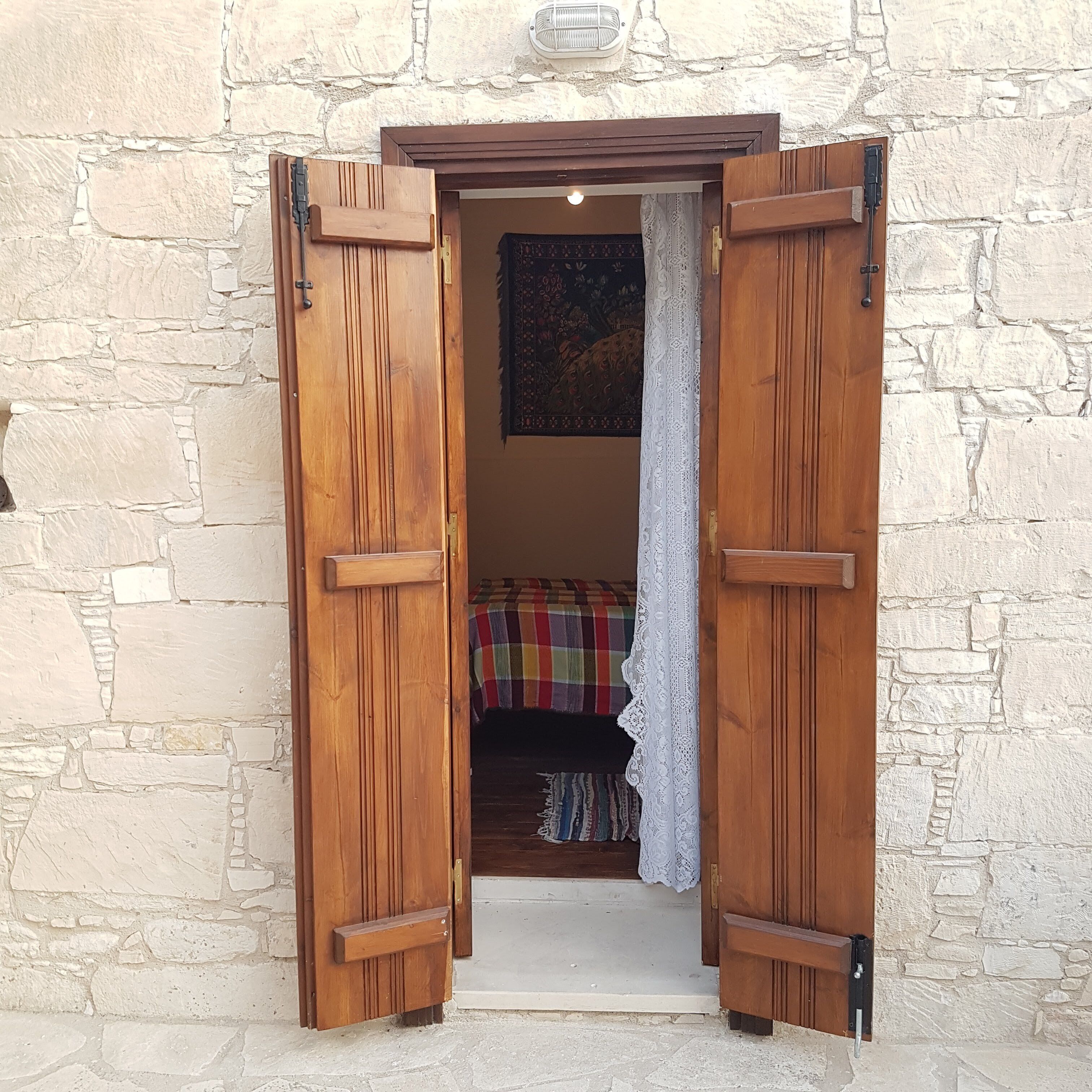Una puerta de madera con un pestillo, que da a una habitación con una cama y un tapiz estampado.