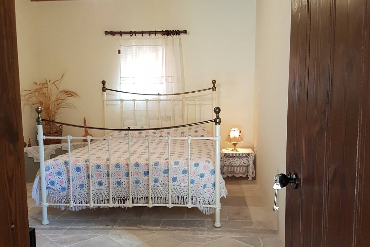A bedroom with a bed, a nightstand, a lamp, and a window with curtains.