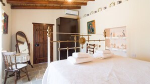 A bedroom with a wooden bed frame, a bedside table, a chair, a wardrobe, and a mirror. - Olympia Traditional Houses (Lympia)