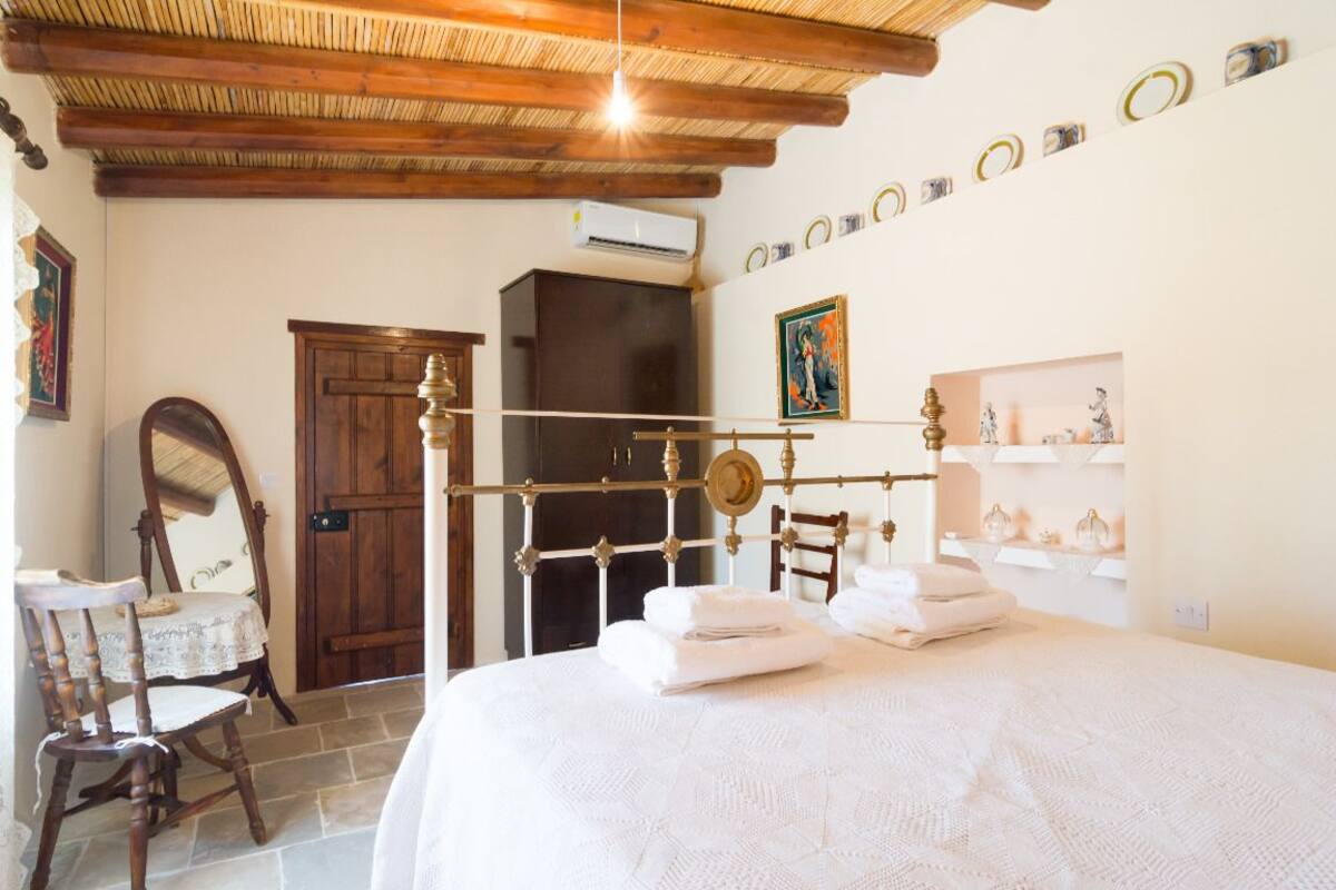 A bedroom with a wooden bed frame, a bedside table, a chair, a wardrobe, and a mirror.