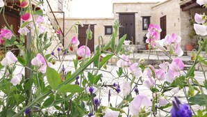 A courtyard with flowering plants and a stone building with a wooden door. - Olympia Traditional Houses (Lympia)