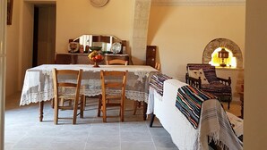 A dining area with a table set for four, surrounded by wooden chairs. A patterned tablecloth covers the table, and a colorful woven blanket is draped over the back of a chair. - Olympia Traditional Houses (Lympia)