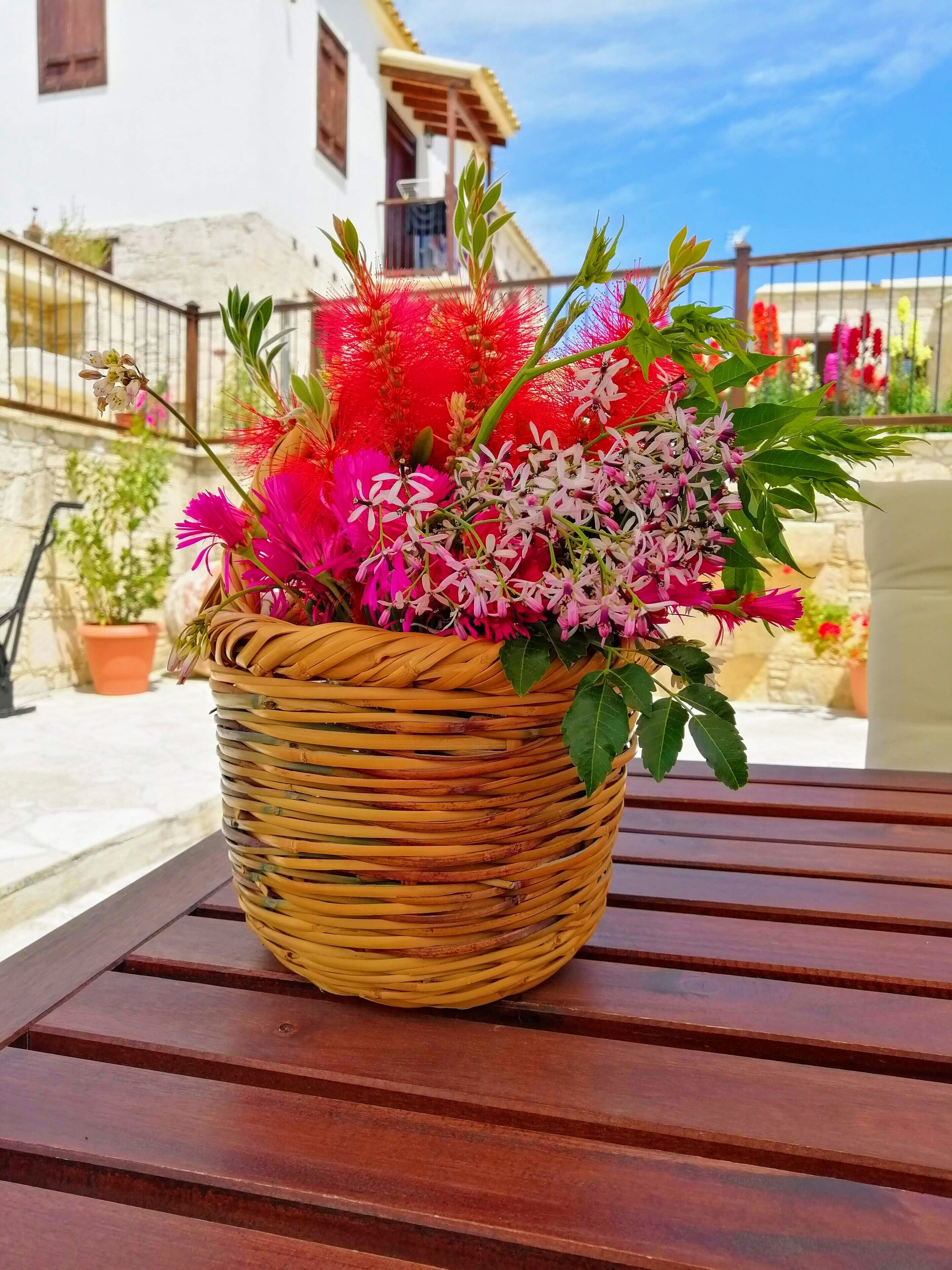 A wicker basket filled with vibrant flowers on a wooden table.