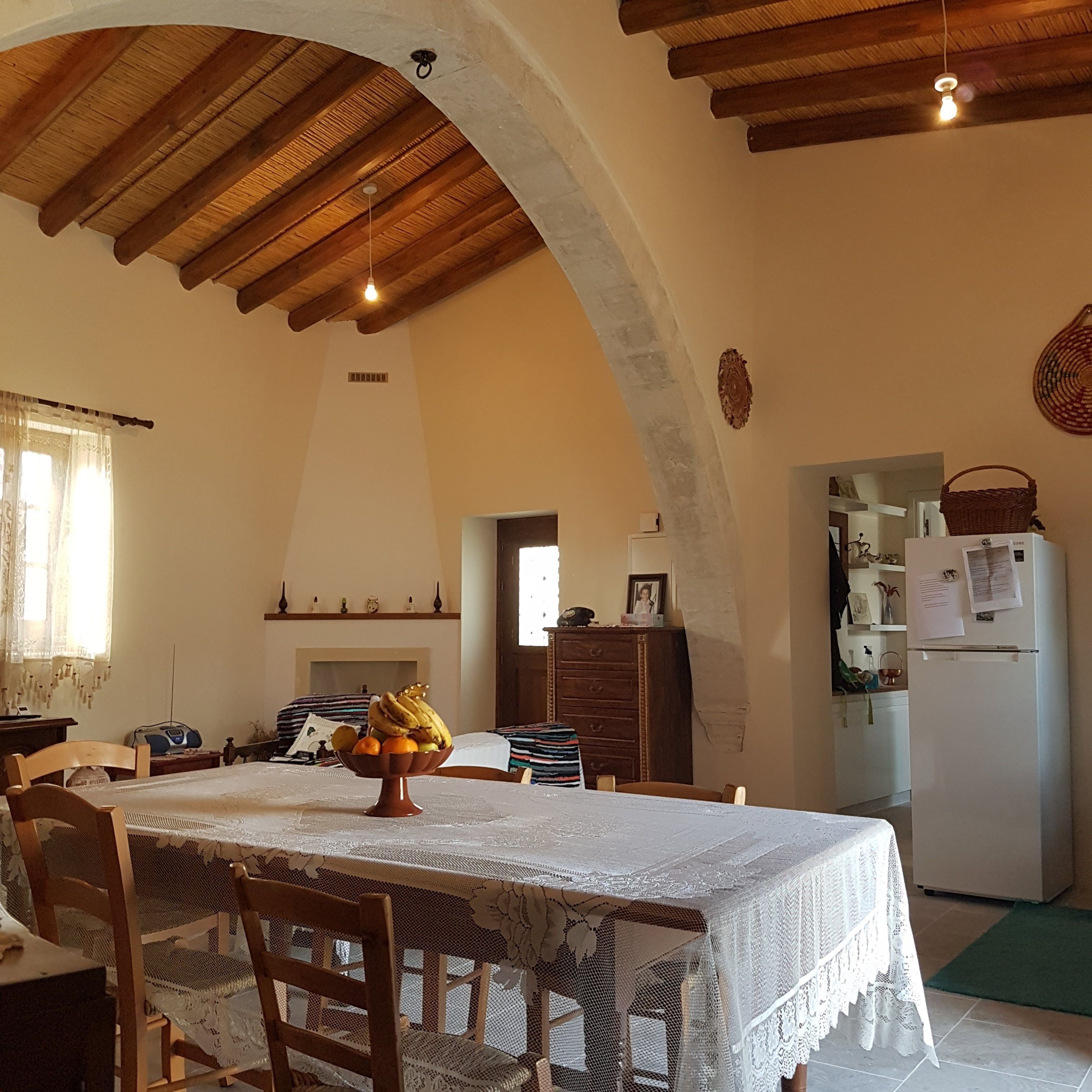 A cozy dining area with a wooden ceiling, a table with a lace tablecloth, and a fruit bowl.