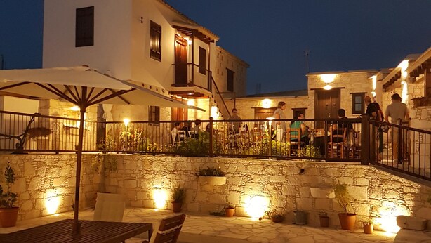 An outdoor patio area with stone flooring, wooden furniture, and potted plants. - Olympia Traditional Houses (Lympia)