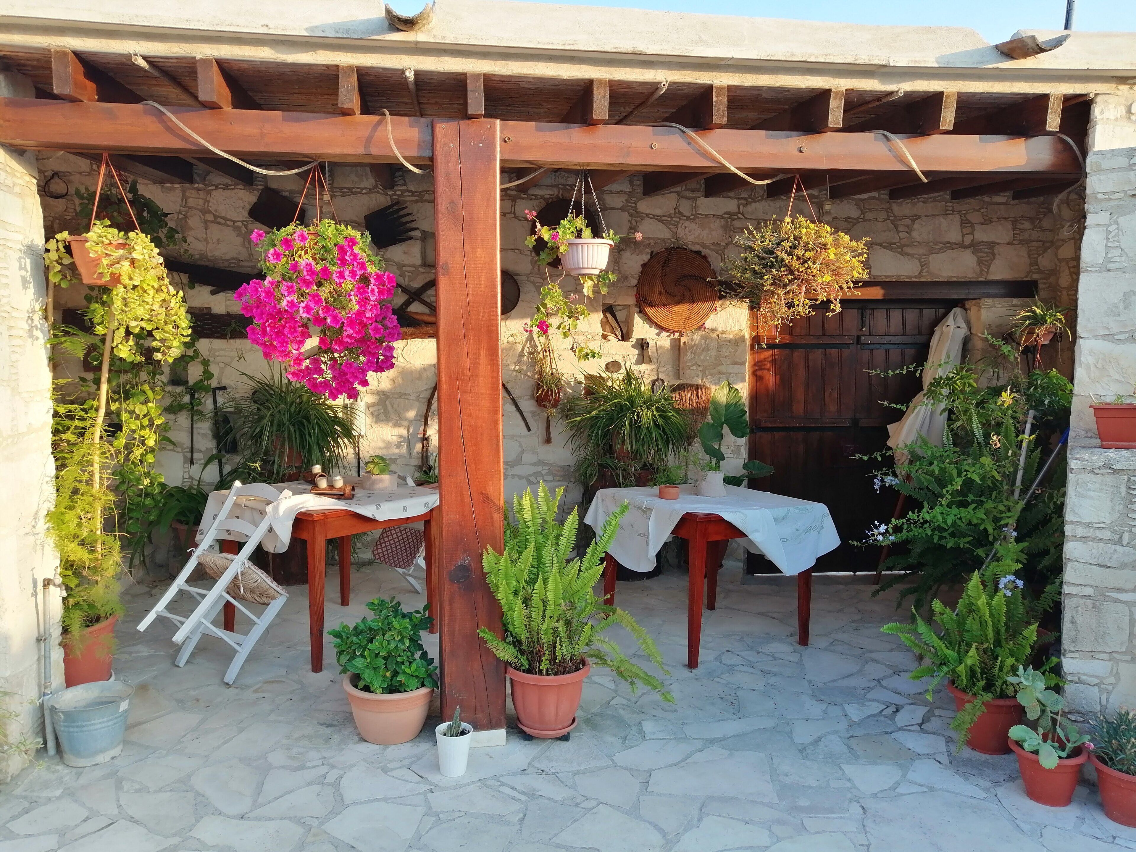 Un espacio al aire libre techado con paredes de piedra, mesas de madera y varias macetas con plantas.