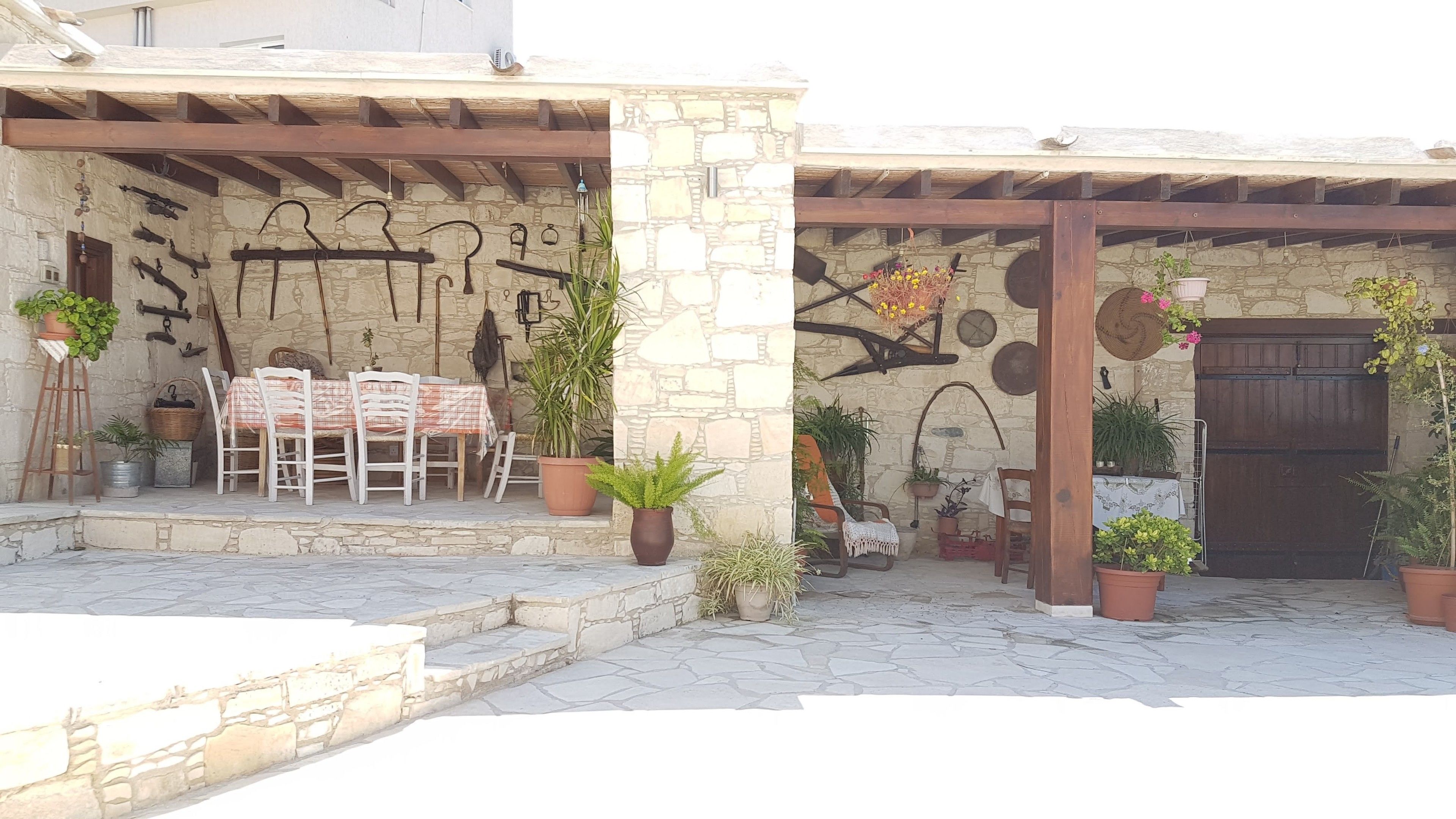 Un espacio de estar rústico al aire libre con muros de piedra, vigas de madera y plantas en macetas.