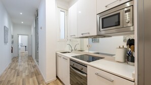 Una cocina moderna con armarios blancos, un microondas de acero inoxidable, horno empotrado y un lavamanos.