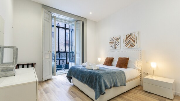 Un dormitorio moderno con cama, mesitas de noche y vistas al exterior.