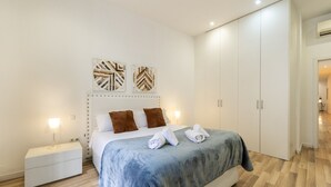 Un dormitorio moderno con una cama grande, mesitas de noche blancas y un armario.