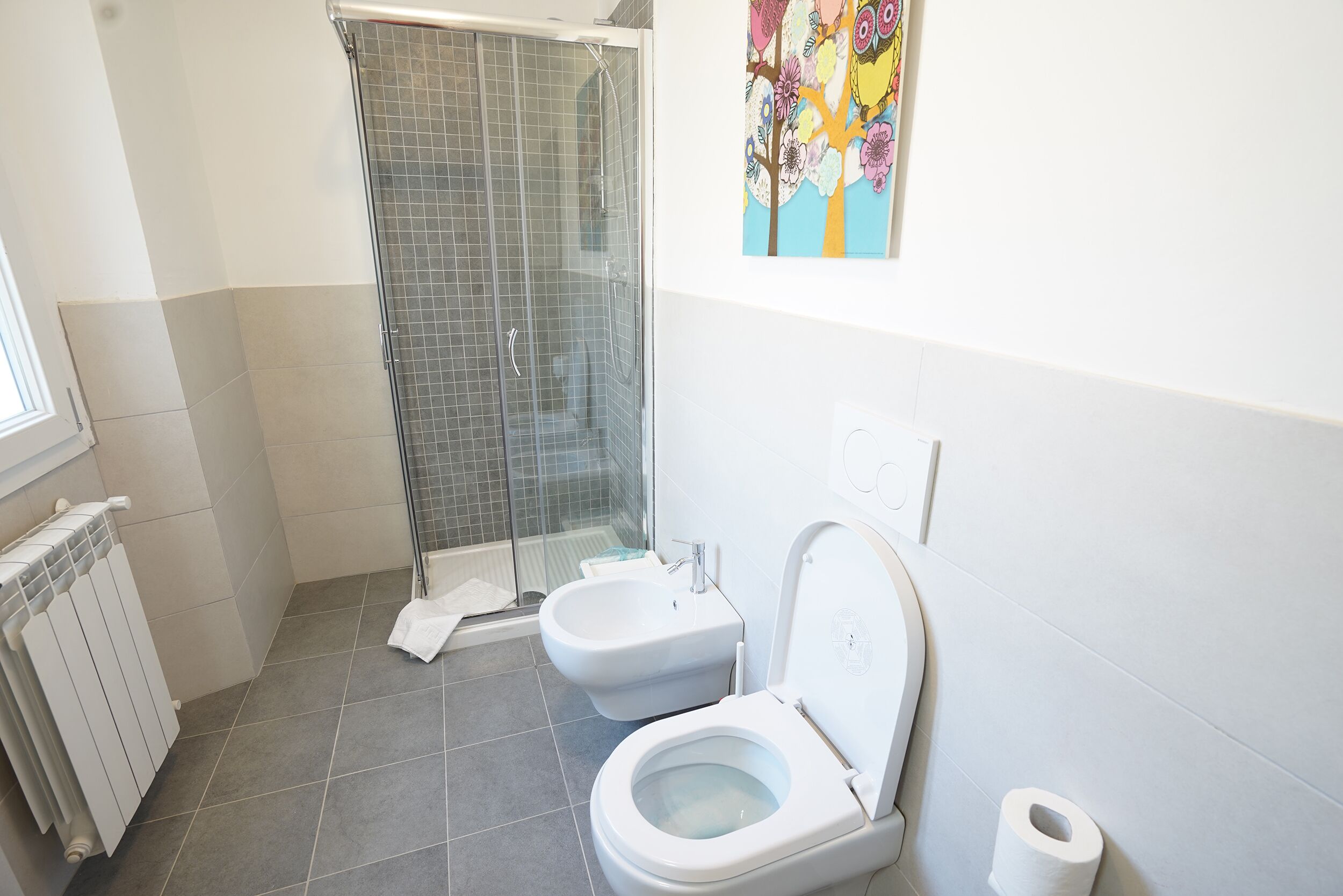 Un baño moderno con ducha, dos inodoros y un radiador.