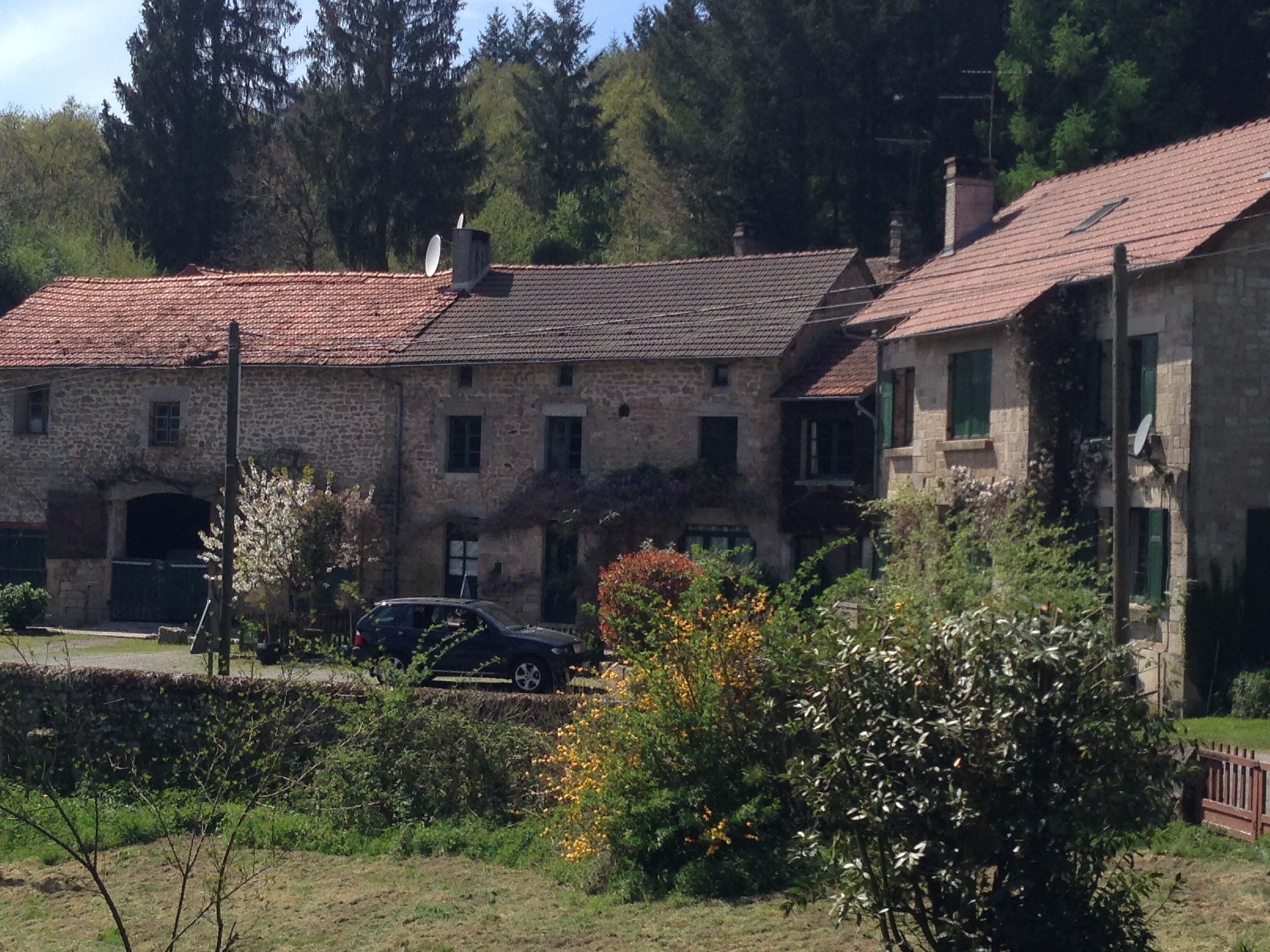 A stone building with a tiled roof, a car parked in front, and surrounding greenery.
