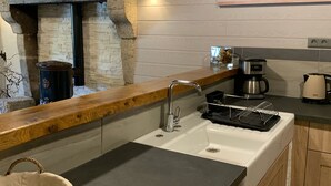 A kitchen with a stone archway, a sink with a dish rack, a coffee maker, and a washing machine. - Charming holiday cottage with shared heated outdoor pool, large garden & BBQ (Saint-Sylvestre)