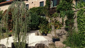 A stone building with a garden in front, including a hanging plant, potted plants, and a small water feature. - Charming holiday cottage with shared heated outdoor pool, large garden & BBQ (Saint-Sylvestre)