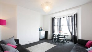 Ein modernes Wohnzimmer mit einer schwarzen Couch, einem grauen Teppich und einem Essbereich mit Tisch und Stühlen.