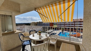 A balcony with a white table, two chairs, a striped awning, and a view of a swimming pool. - Blaumar B38 Estartit apartment rental with pool and air conditioning (Estartit)